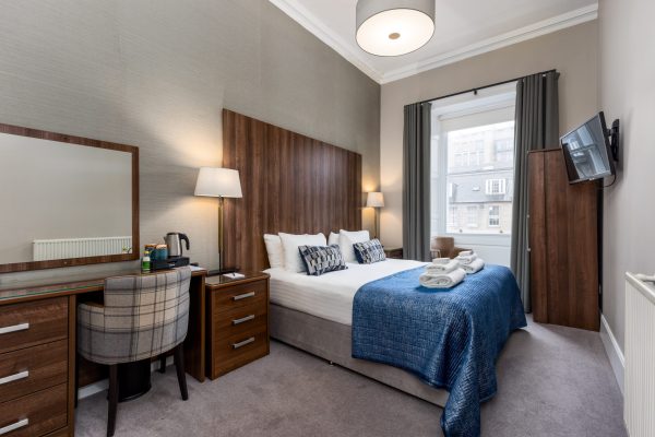 Hotel bedroom at 28 York Place with a wooden headboard, blue tartan throw, and desk area.