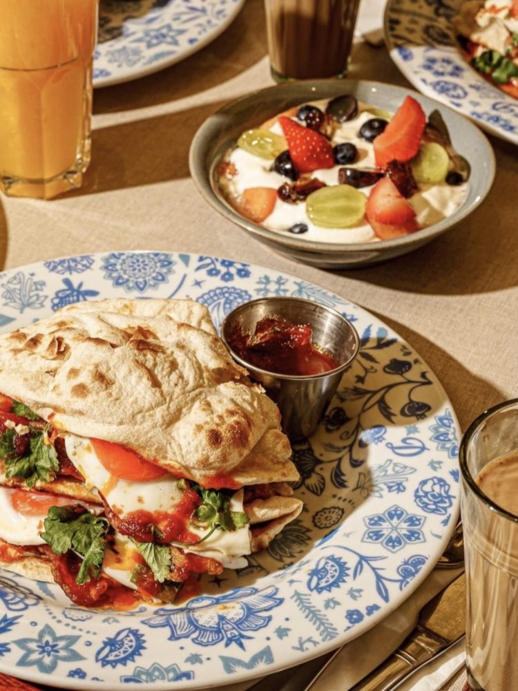 Dishoom breakfast spread with a bacon naan roll, yoghurt with fresh fruit, chai and orange juice in Edinburgh