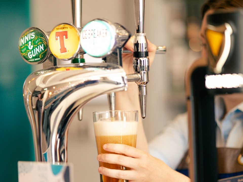 A bartender pours a pint of beer from the taps at Bar28, with a drinks menu on the counter.