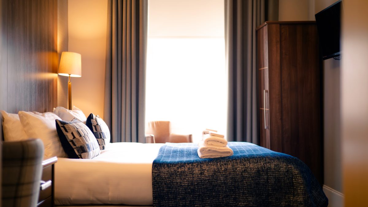 Hotel bedroom at 28 York Place with a bed, folded towels, lamp, and curtained window.