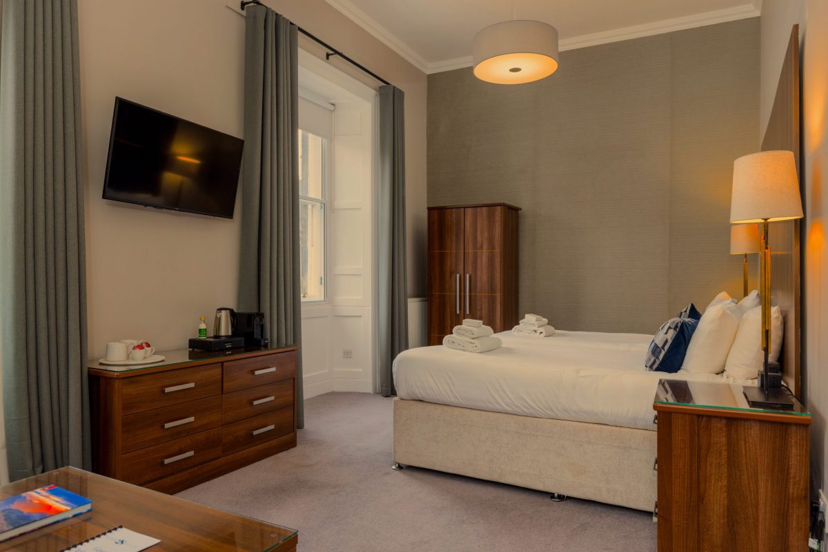 Hotel bedroom at 28 York Place with a double bed, wall-mounted TV, and wooden furnishings.