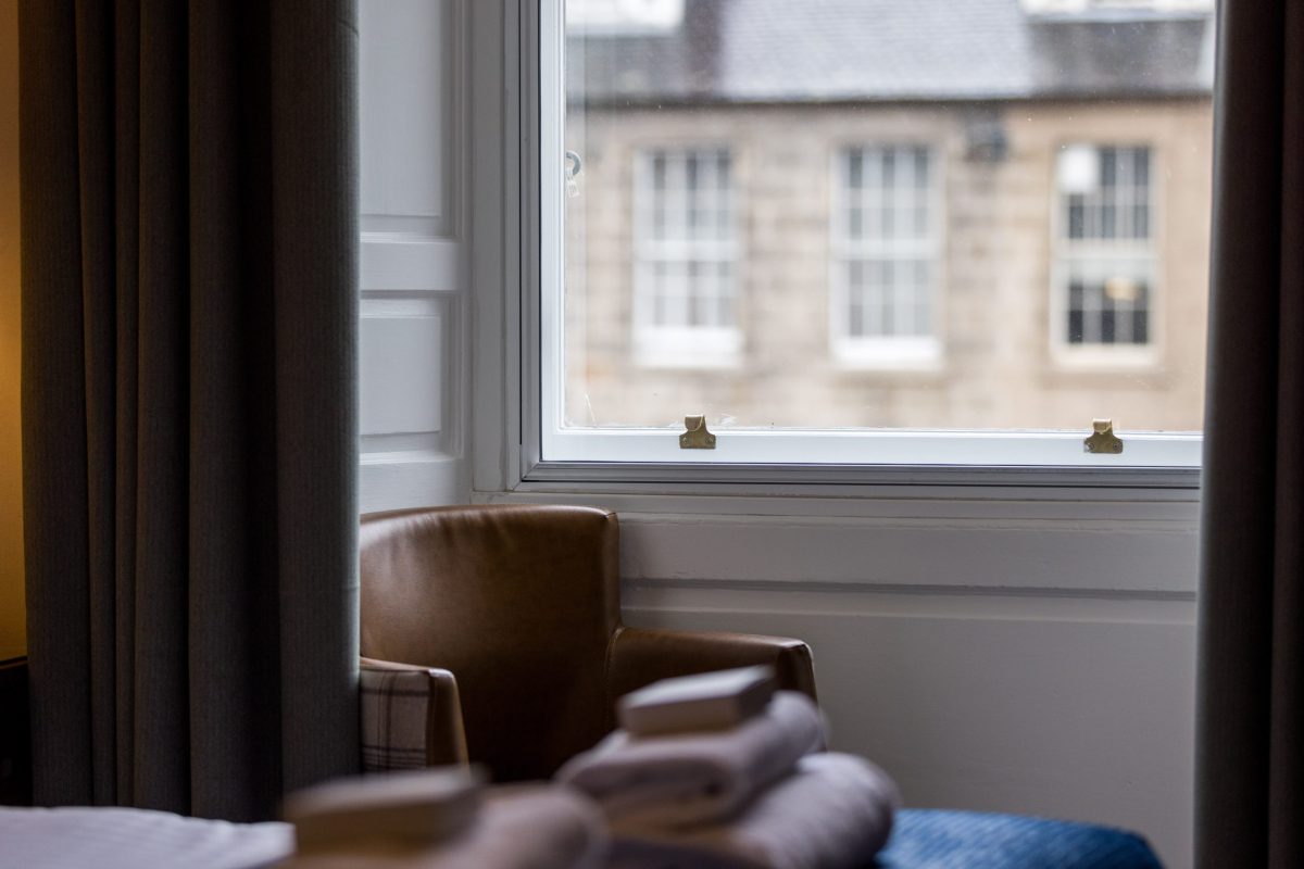 Hotel room window at 28 York Place with a view of New Town sandstone buildings, towels and armchair in the foreground.